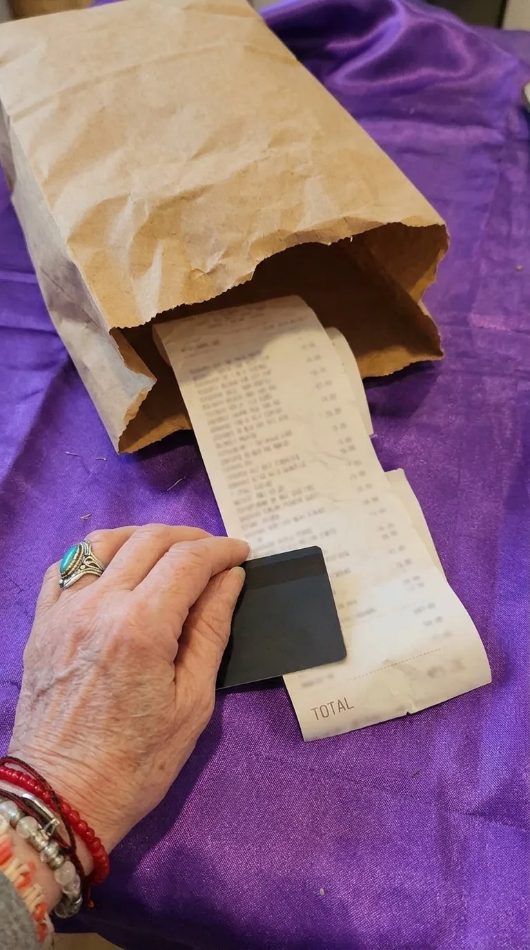 Una bolsa de compras con un ticket largo y una tarjeta bajo la mano